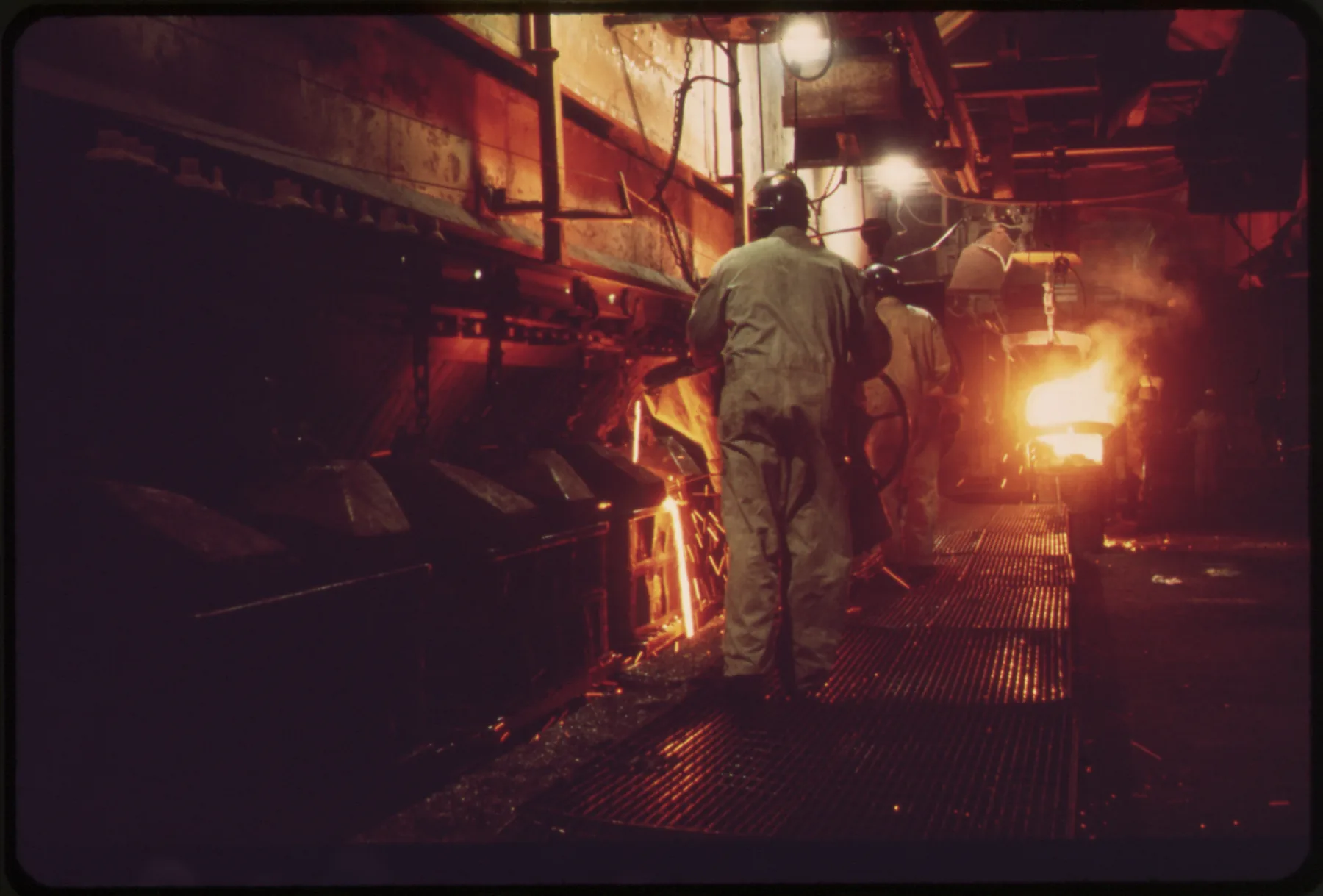 Workers pouring molten metal into sand moulds in an industrial foundry